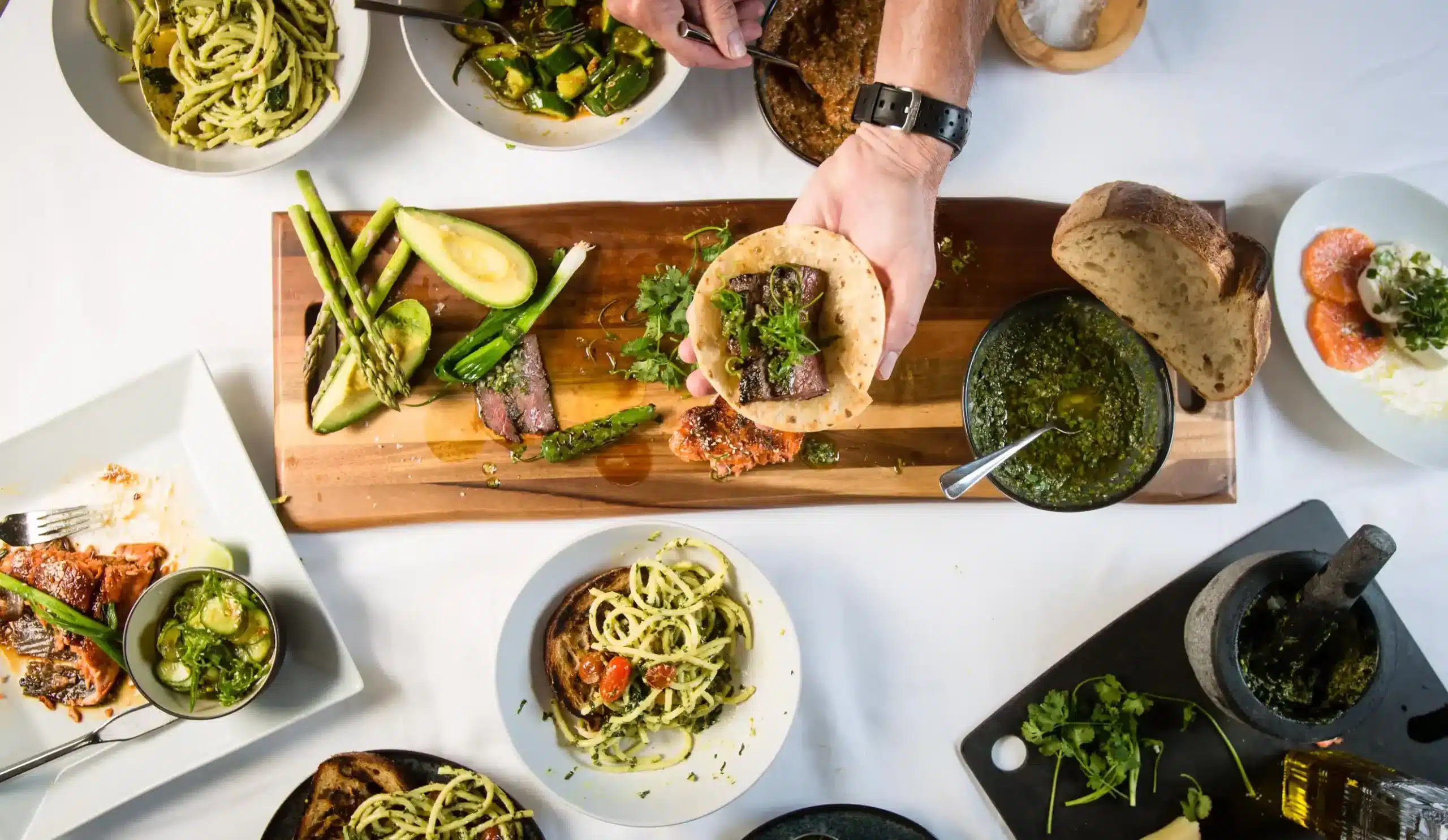Chef assembling a steak flatbread alongside freshly prepared dishes